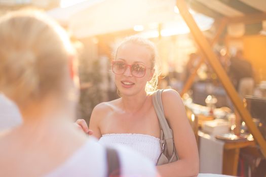 It is nice to see you. It has been a while. Two happy young female friends enjoying a conversation on urban food market at random after work encounter. Pleasant free time socializing.