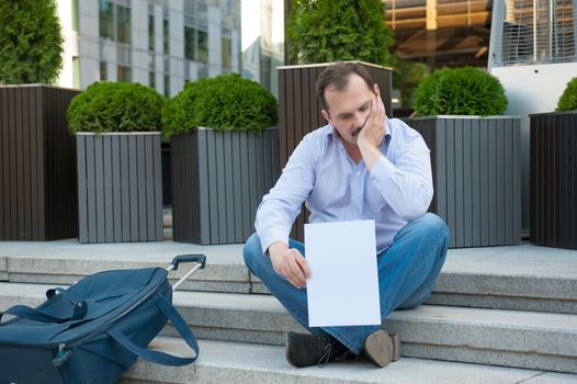 Sad man sitting on the steps with a suitcase Empty sign outdoors