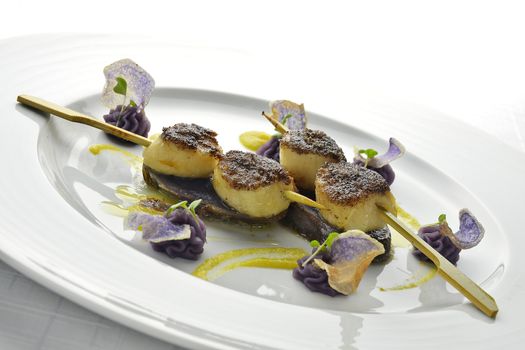 Fish Dish Skewer of Scallops Crusted with black Rice and Purple Potatoes in white plate