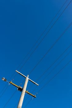 Power pole and power lines with a street light on blue sky.