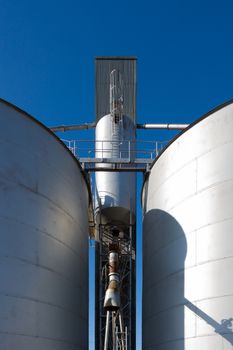 Shot taken of two silos and their drop tube inbetween.against blue sky.