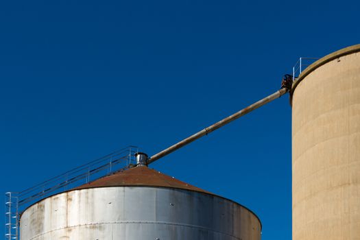 A close up of the top of large silos on a blue sky.