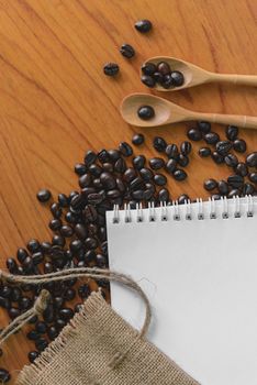 White notebook for your text with sackcloth and coffee beans on wooden spoon.