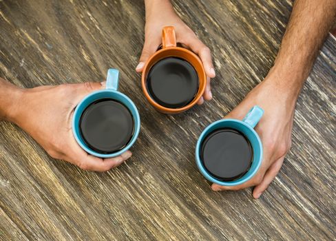 Hands holding cups of coffee over a table