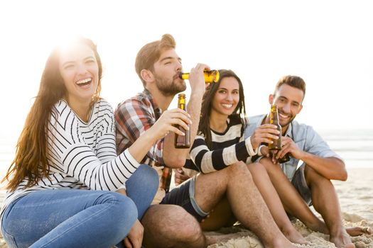 Friends having fun together at the beach and drinking a cold beer