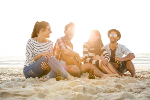 Friends having fun together at the beach, playing guitar and drinking beer