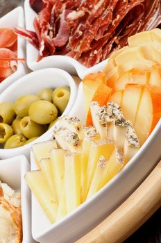 Serving Plate with Delicious Spanish Cheeses, Cured Ham, Green Olives and Bread closeup. Focus on Foreground