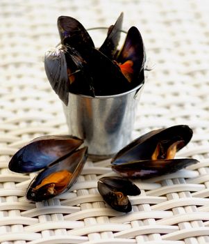Tin Bucket with Delicious Boiled Mussels closeup on Wicker background. Focus on Foreground