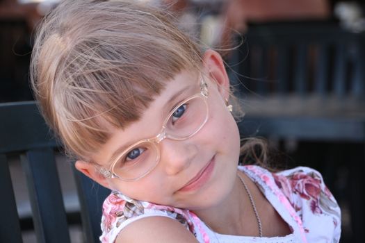 Smiling little blond girl with glasses bent her head