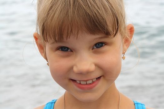 portrait of smiling little funny blonde girl on blue sea background