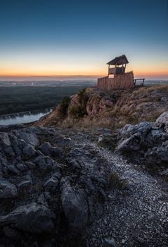 Wooden Tourist Observation Tower on Rocky Hill over a Landscape with a River at Dusk
