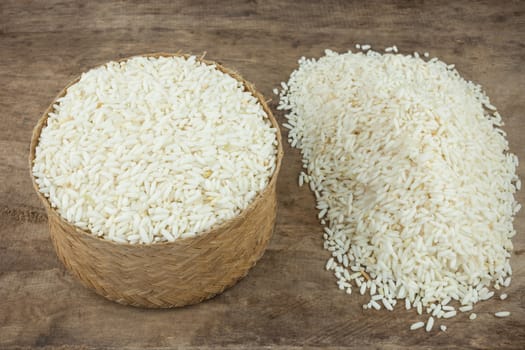 Rice in a wicker rice and scattered near on dark wooden table.