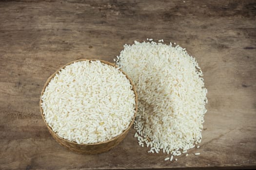 Rice in a wicker rice and scattered near on dark wooden table.