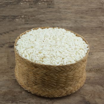 Rice in a wicker rice and scattered near on dark wooden table.
