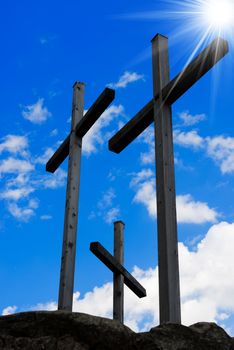 Three wooden crosses on a blue sky with clouds and sun rays on a hill. Symbol of Jesus crucifixion