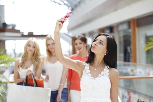 Happy woman with bags taking selfie in shopping mall
