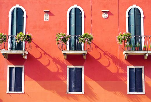 three doors with terrace and three windows on orange wall building in Venice, Italy