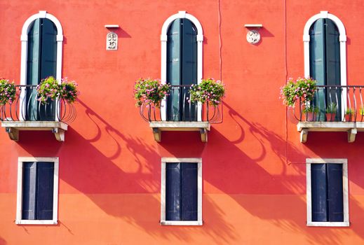 three doors with terrace and three windows on orange wall building in Venice, Italy