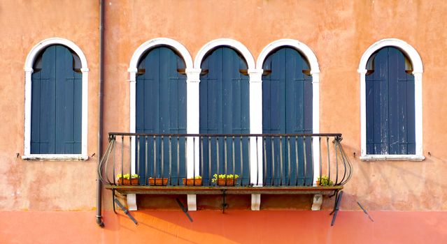 three doors with terrace and two windows on orange wall building in Venice, Italy