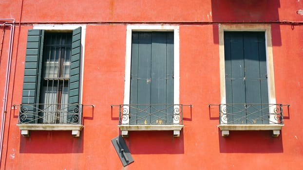 three wiindows on orange wall building in Venice, Italy