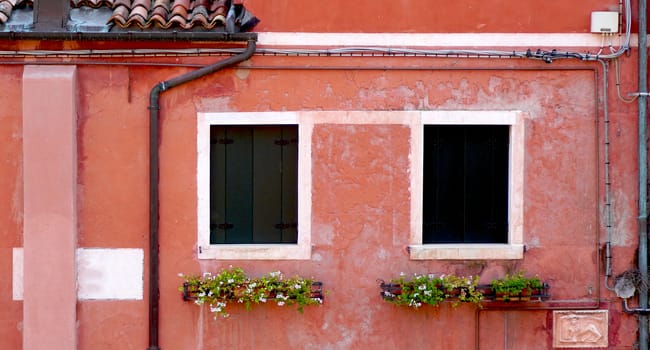 two windows and drained pipe with coral color wall house building in Venice, Italy