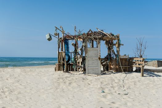 Remnants of a ruined beach or fishing hut with a closed wooden door in a tattered timber framework without walls standing in golden beach sand overlooking the sea, possibly the aftermath of a typhoon