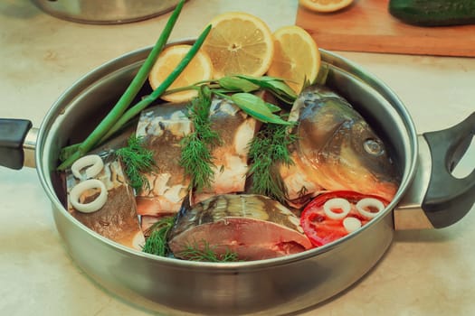 In a large skillet, stainless steel is chopped fish and ingredients for cooking: vegetables, lemon, onion, dill.