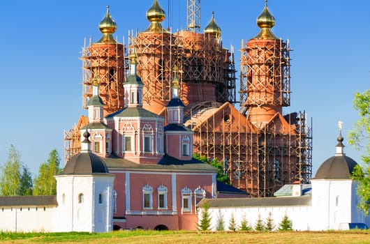 Behind a monastery wall visible to erect a temple with gold domes in scaffolding.