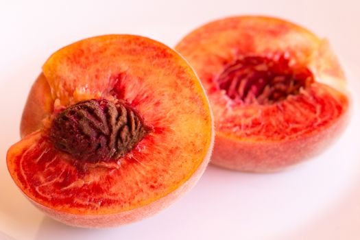 One mature peach, cut in half, on a white background.