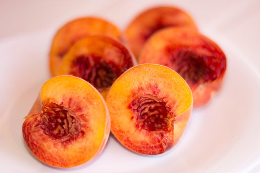 Three mature peaches cut in halves, on a white background.