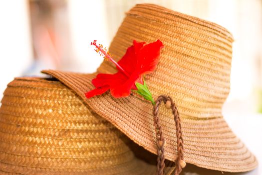 Two straw hats on a white table, with an hibiscus flower on one of them.