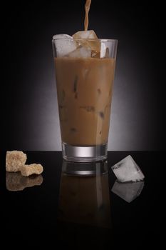 Ice coffee with melting ice cubes and brown sugar on dark background. Culinary gourmet luxurious coffee drinking.