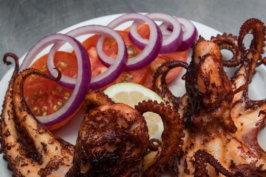 fried octopus served with tomatoes and onion on white plate