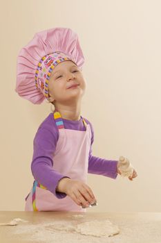Little girl in chef hat and tablier with classic wooden rolling pin, dough and flour. Gastronomy and culinary cooking.