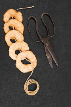 Dry apple slices on black background, with old vintage scissors and natural brown string. Healthy eating, seasonal harvest conservation.