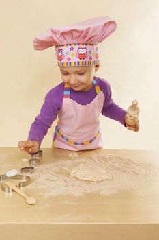 Little girl in chef hat and tablier with classic wooden rolling pin, dough and flour. Gastronomy and culinary cooking.