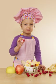 Little girl in purple cook hat and tablier making fruit salad. Healthy eating habits. 