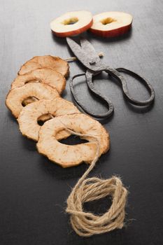 Dry apple chips on black background, with old vintage scissors and natural brown string. Healthy eating, seasonal harvest conservation.