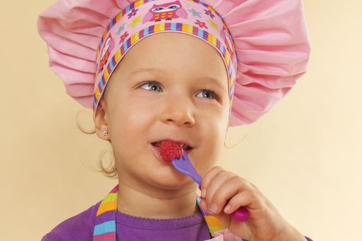 Little cute girl with chef hat eating raspberry. Culinary concept.