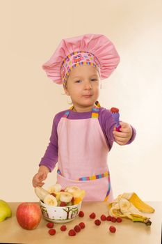 Little girl in purple cook hat and tablier making fruit salad. Healthy eating habits. 