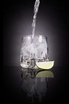 Drinking vodka. Pouring vodka into luxurious shot glass with lime on black background with reflection. Traditional transparent alcohol drinking.