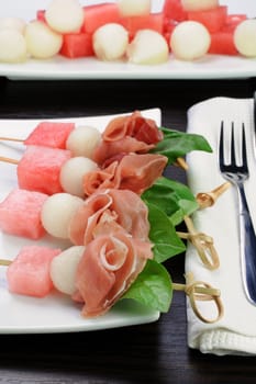 Appetizer of ham with melon and watermelon and basil on a skewer