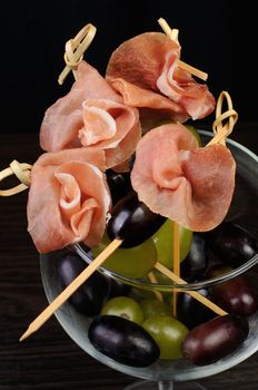 Appetizer of ham with grapes on a skewer in the glass