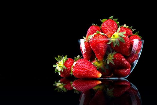 Delicious strawberries in a glass bowl on black background.