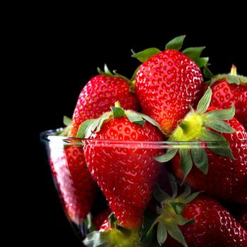 Delicious strawberries in a glass bowl on black background.