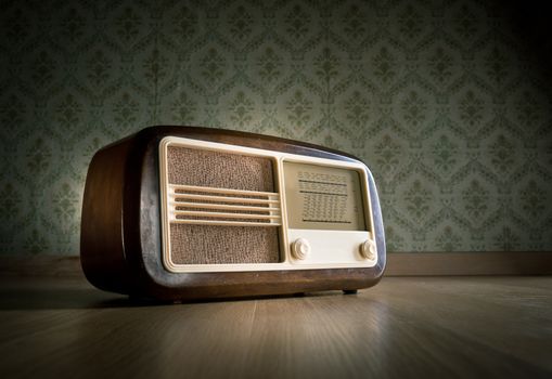 Old vintage radio on hardwood floor with retro wallpaper on background.