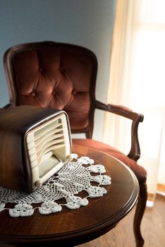 Vintage radio on round table with doily and living room on background.