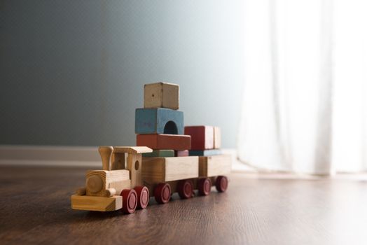 Vintage wooden toy train next to a window on hardwood floor.