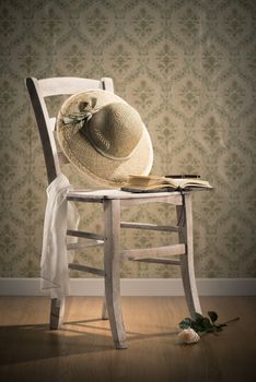 Old open book and straw hat on a shabby chic chair and rose on floor.