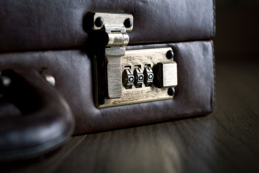Leather briefcase lock and handle close-up on dark hardwood floor.